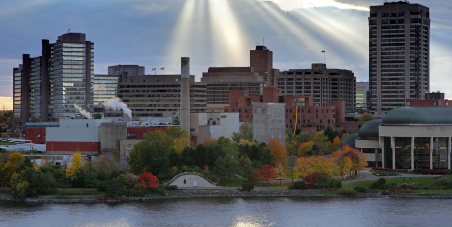 Foundation repair services provided in Gatineau. Skyline of Gatineau, Quebec, with sunlight streaming through the clouds, highlighting the city's buildings and the surrounding greenery near a river.