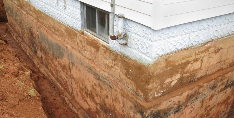 A partially excavated basement foundation of a house, showing exposed soil and lower sections of the foundation walls during a basement lowering process trying to increase basement ceiling height