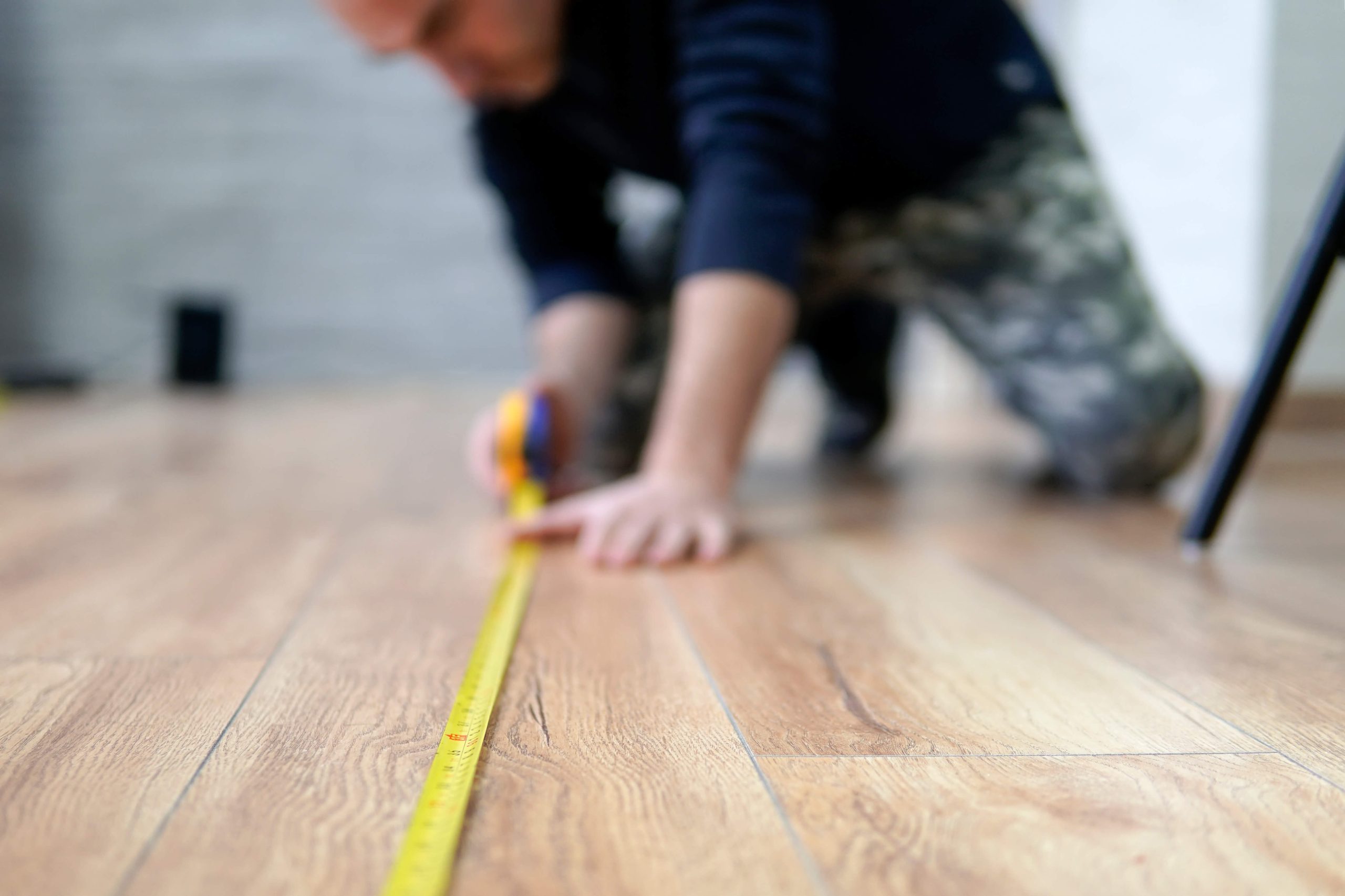 Close-up of a professional measuring an uneven floor with a tape measure, highlighting flooring issues and repairs.