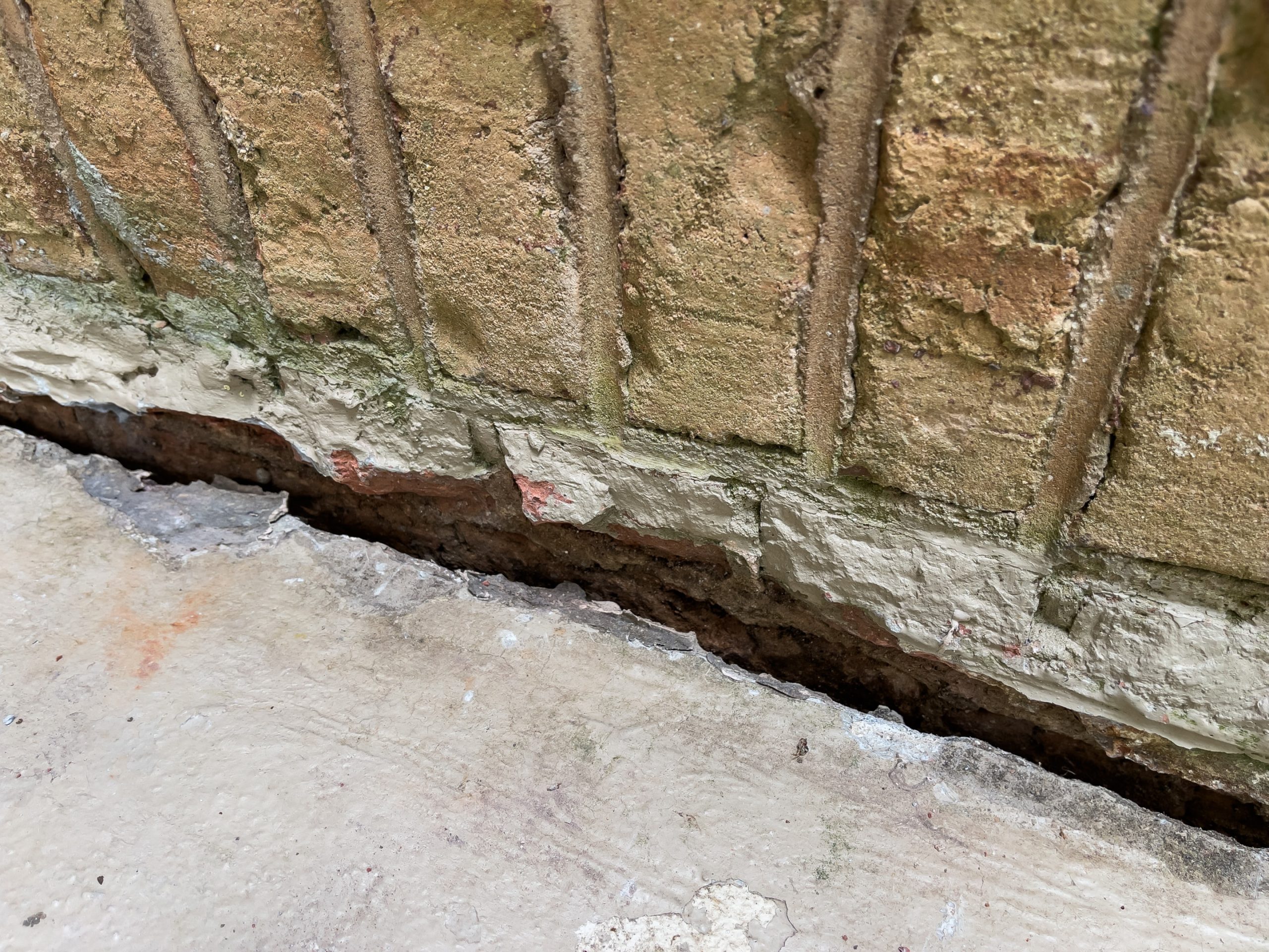 How to fix a sinking foundation – gap between a concrete slab and brick wall showing settlement.